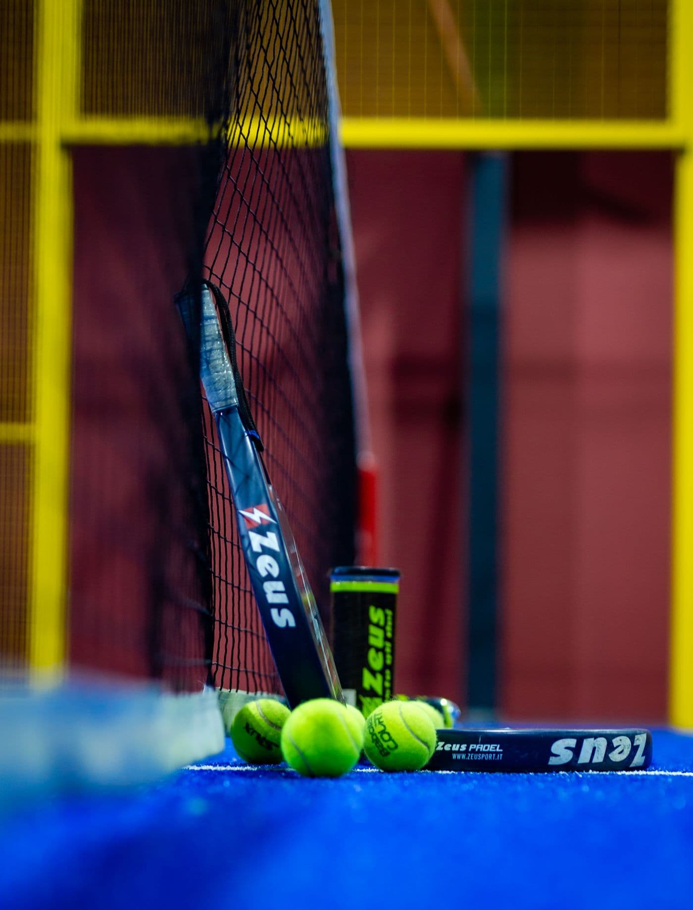 Padel racket and lime balls resting beside the net on a blue court