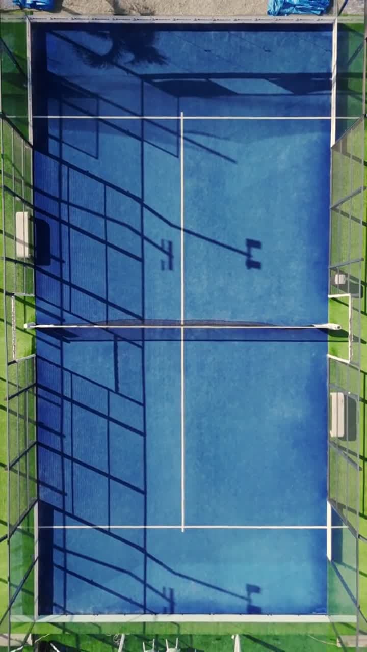 Overhead view of a blue Padel court, its net and glass enclosure